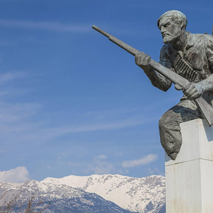 War memorial monument with bronze soldiers and snow-covered mountains in the background