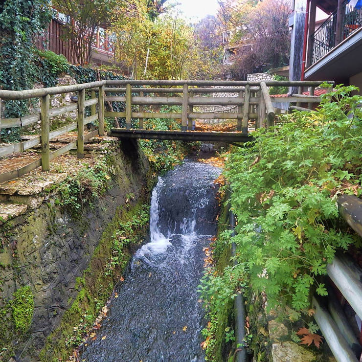 Wooden bridge and small waterfall flowing through the picturesque village of Arogiani