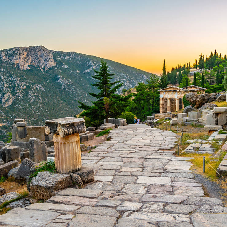 Ancient ruins of the Temple of Apollo in Delphi at sunset with mountain backdrop