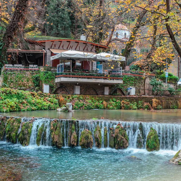 Riverside cafe by the Erkyna stream in Livadeia, surrounded by greenery and gentle waterfalls