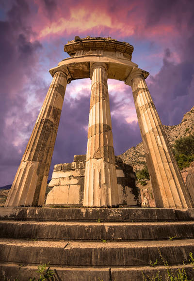 Ancient Tholos of Delphi with marble columns under a dramatic purple sunset sky