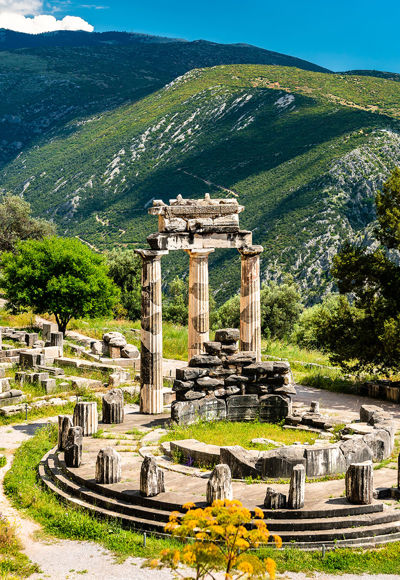 Marble columns of the Tholos of Delphi surrounded by ancient ruins and greenery