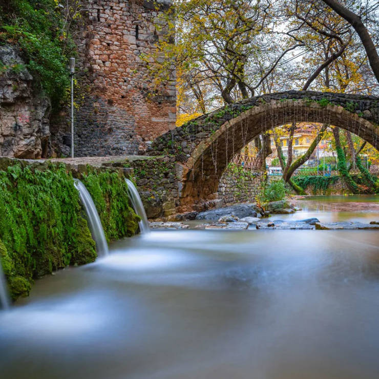 Stone arched bridge over Herkyna stream with small waterfalls in Livadeia